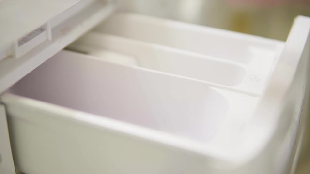 A close up detail of purple laundry detergent poured into a washing machine.