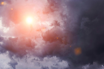 Dramatic storm dark grey cumulus clouds with orange sun and sunlight	