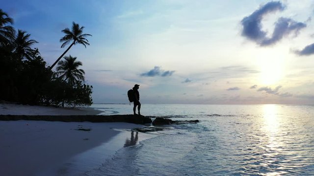 Silhouette of a tourist enjoying the beauty of the pristine nature. Beautiful purple sunrise over the tropical sandy beach with palms.
