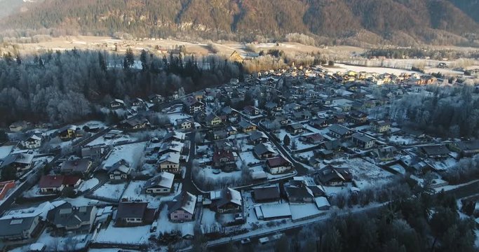 Small mountain village under the snow with mountain peaks in the background. Aerial revealing shot. Ramsau, Austria