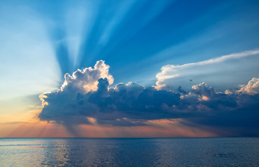 Magnificent sunset over sea. Sun covered by picturesque cloud with beautiful shine sun beams in sky