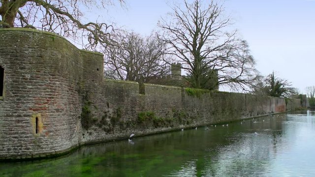 Over the moat, looking towards the imposing walls and castle towers of the Medieval Bishop's Palace in Wells, UK
