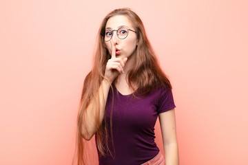 yound blonde woman asking for silence and quiet, gesturing with finger in front of mouth, saying...