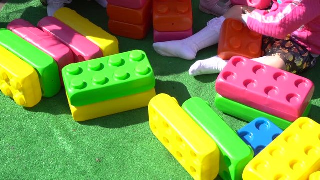 Closeup view of many bright colorful plastic toy bricks and little babies playing them outdoor on sunny spring or summer day.