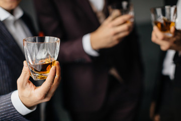 Close-up partial view of three friends clink glasses of whiskey drink, alcoholic beverage. Whisky drink