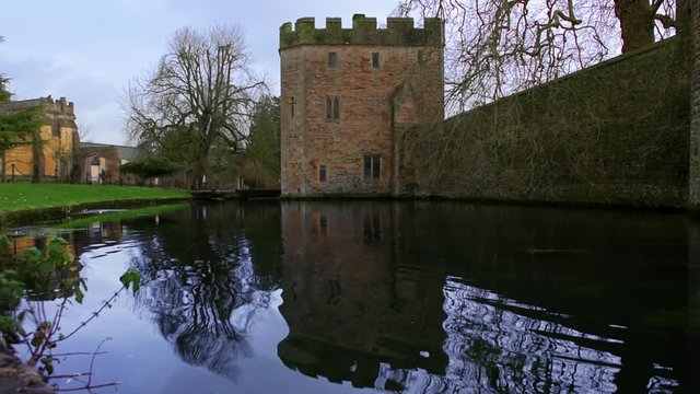 A low shot across the moat toward the wall and main gate tower of the Medieval Bishop's Palace castle in Well, UK