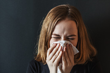 Sick young woman, with wrinkled nose, blowing her nose and fever, caught a cold, sneezing in...
