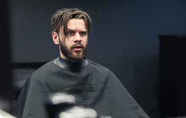 Scared look. Close up photo of a bearded man with messy hair who is looking at his reflection in a barbershop mirror with a scared facial expression.