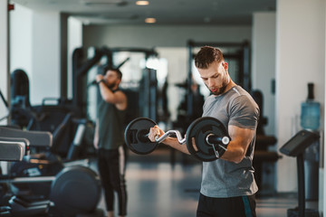 Young bearded man doing biceps exercises  in gym with barbell