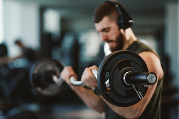 Fototapeta na wymiar Young bearded man doing biceps exercises in gym with barbell selective focus on weights