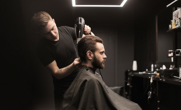 Special day. Side view low angled photo of a barber stylist, who is drying hair of his client, using a special round comb.
