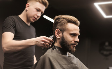 Shaving back of the head. Side view low angled photo of a young barber trimming customer’s nape with an electric shaver.