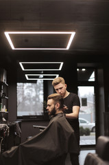 Barber’s day. Profile photo of a young barber taking care of his customer’s hair, using an electric shaver.