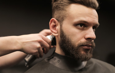 Fototapeta premium A confident look. Close-up shot of a young masculine man who is having his hair trimmed with an electric razor by a professional barber.