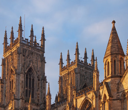 a rear view of the towers at the entrance to york minster in sunlight against a blue cloudy sky