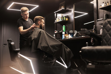 Visit the barbershop. Side view photo of a man, who is cutting hair of his special client in a...