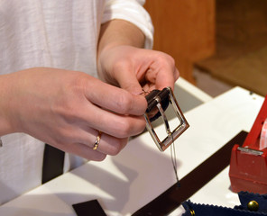 young craftswoman putting the metal buckle on a leather belt