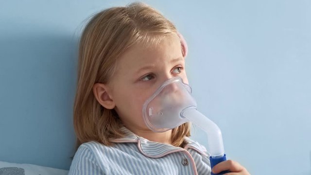 Сhild is sick and breathes through an inhaler. Little girl treats flu by inhaling inhalation vapor. Toddler asthma inhaling mask illnesses.