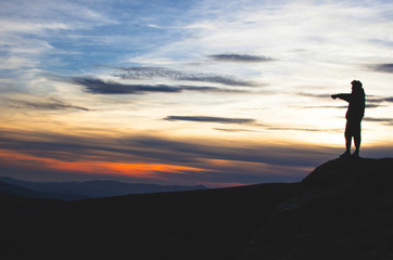 Fototapeta na wymiar man on top of a mountain points the horizon towards a mountain landscape at sunset
