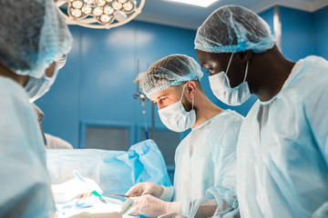 An international team of doctors performs a complex surgical operation on a patient under anesthesia. Modern operating room and experienced surgeons save lives