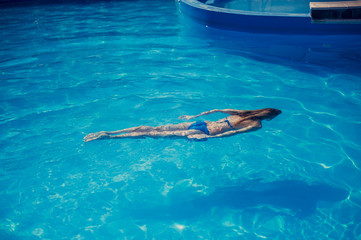 Young slim woman in a black bikini swimsuit swims underwater in the pool