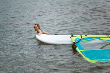 A girl in the water of the sea swims and pulls board with a sail for windsurfing