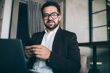 Serious ethnic director watching cellphone at workplace