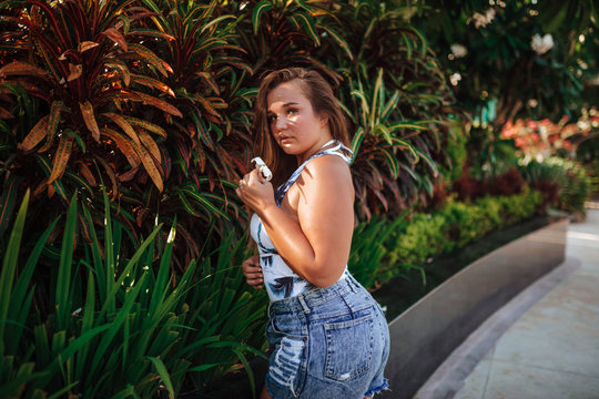 Girl, xxl size model, plump girl in a white one-piece swimsuit and blue jeans shorts posing in the green in the jungle