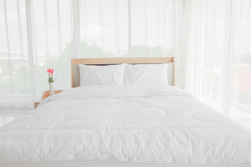 Bedroom interior with bed and flowers on nightstand.White bedroom interior with double bed on a floor