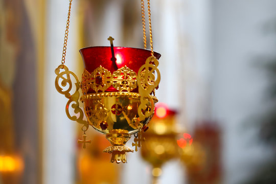 Orthodox Church Church lamp with a lit candle and red glass in a gold case hangs in front of icons