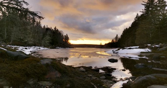 Sunset at the mouth of a Beautiful rocky and ice covered cove surrounded by dead fall pine trees in rural Nova Scotia, Canada
