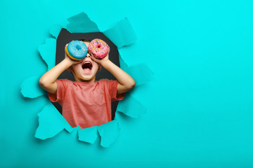 Happy cute boy is having fun played with donuts on black background wall. Bright photo of a child.