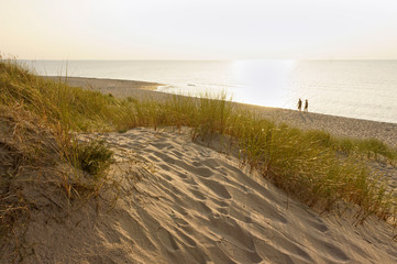 Fototapeta na wymiar Sand dunes and sea sunset. Walk on the evening sea.
