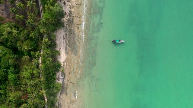 Aerial drone view of traditional longtail boats next to a beautiful tree lined tropical beach (Khao Lak, Thailand)