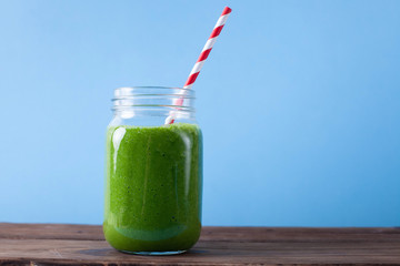 Fresh green smoothie on wooden and blue background. 