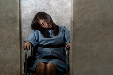 young crazy and mentally insane Asian woman restrained in wheelchair at mental hospital suffering...