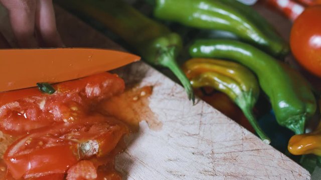 Bad knife squishing tomatoes instead of cutting them on a wooden board with veggies on the background