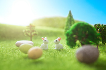 Fototapeta na wymiar Two rabbit toys with easter eggs on a meadow grass. Yellow easter egg spring meadow with two rabbit and easter eggs. Fairy tale