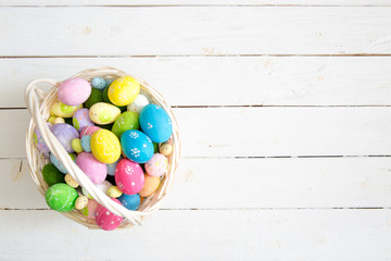 Colorful easter eggs in basket and flowers on white wooden table. Top view with copy space