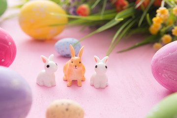 Composition with Easter eggs with rabbits or hare toys and flowers on pink wooden background