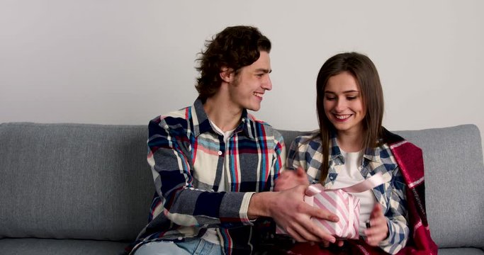 Couple sitting on sofa, giving presents to each othes and smiling in valentine day