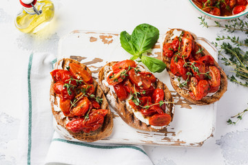 Sandwiches with baked cherry tomatoes and cottage cheese, thyme, garlic and herbs on an old light vintage background. Top view.