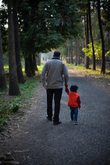 Backside of an Indian brunette father and his baby boy in winter garments walking in a forest path in winter afternoon in natural green background. Indian lifestyle and parenthood.