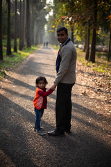 Obraz premium An Indian brunette father and his baby boy in winter garments standing on a forest path in winter afternoon in natural green background. Indian lifestyle and parenthood.