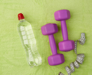 purple dumbbells and a clear plastic bottle of water on a green terry towel
