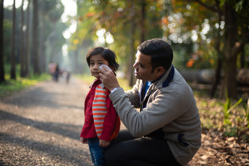 An Indian brunette father taking care of his baby boy in a path surrounded by green forest in winter afternoon in green natural background. Indian lifestyle and parenthood.