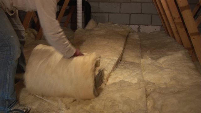 Man rolling out soft rockwool type insulation in the roof / Attic / Loft of his house - Stock Video Clip Footage