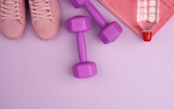 purple dumbbells and a clear plastic bottle of water, pink shoe on a terry towel, top view, flat lay © nndanko
