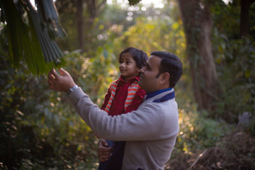 Obraz premium An Indian brunette father and his baby boy in winter garments enjoying themselves in winter afternoon on a dry grass field in green natural background. Indian lifestyle and parenthood.