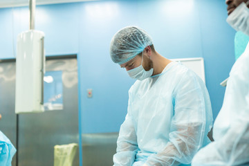 Portrait of a tired surgeon in medical uniform and mask after the operation is completed, bowed and rests